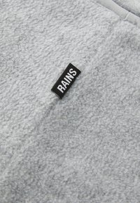 Light grey fleece fabric featuring a textured surface with a black label reading "RAINS" stitched on the side.