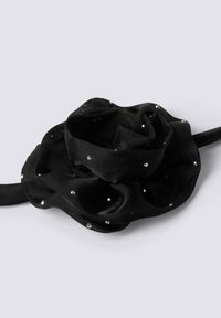 Accessorio floreale in tessuto nero con petali sovrapposti adornato con piccole pietre di strass trasparenti, attaccato a una fascia nera.