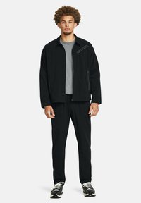 Chándal deportivo negro que incluye una chaqueta con cremallera y bolsillos laterales, una camiseta interior gris y pantalones ajustados a juego. Tejido texturizado.