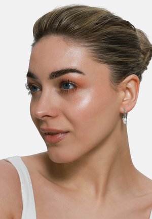 Silberne Creolenohrringe mit einem Cluster aus strukturierten, glänzenden Perlen. Das Model hat einen glatten Teint und dezentes Make-up, das den Schmuck hervorhebt.