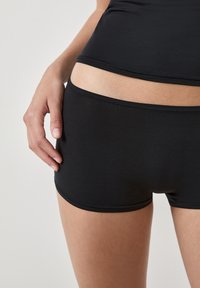 Pantalones cortos negros ajustados en una tela suave y elástica. Diseño limpio con una textura suave y una cinturilla baja, con detalles de costuras sutiles.