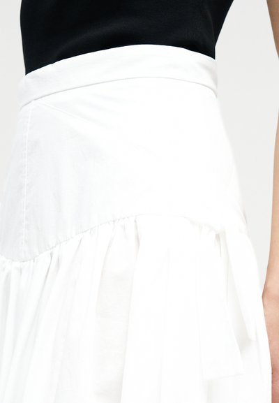 Λευκή ψηλόμεση φούστα με λεπτομέρεια ραμμένης υφής στη ραφή, φορεμένη με μαύρο τοπ.