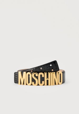 Cintura di pelle nera texturizzata arrotolata con grandi lettere dorate lucide MOSCHINO come fibbia, su sfondo bianco semplice.