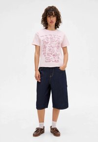 Pink short-sleeve T-shirt with graphic illustrations in red, paired with dark blue denim bermuda shorts. Brown footwear with laces.