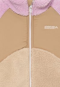 Fleece jakna s kremastim i svijetlopinkim panelima, zatvaračem sa munje i detaljem loga na prsima. Mekana tekstura s različitim materijalima.