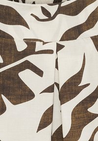 Brunt och krämfärgad tyg med ett abstrakt bladmönster, med en texturerad yta och plisserade designelement.