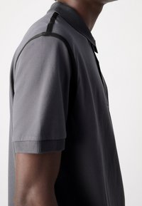 Polo gris en tissu lisse, avec un col et des manches côtelés. Coutures d'épaule discrètes avec des accents contrastants.