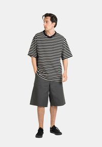 Striped black and white short-sleeve t-shirt with a loose fit; paired with knee-length gray shorts and black sneakers.