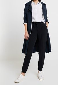 Marinkappa med vit kant, ljusblå skjorta och svarta byxor. Vita sneakers ger kontrast. Slät tygkvalitet och avslappnad passform genom hela plagget.