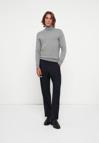 Gray turtleneck sweater and dark trousers, both fitted. Sweater has a smooth texture; trousers are slightly structured. Black shoes complete the outfit.