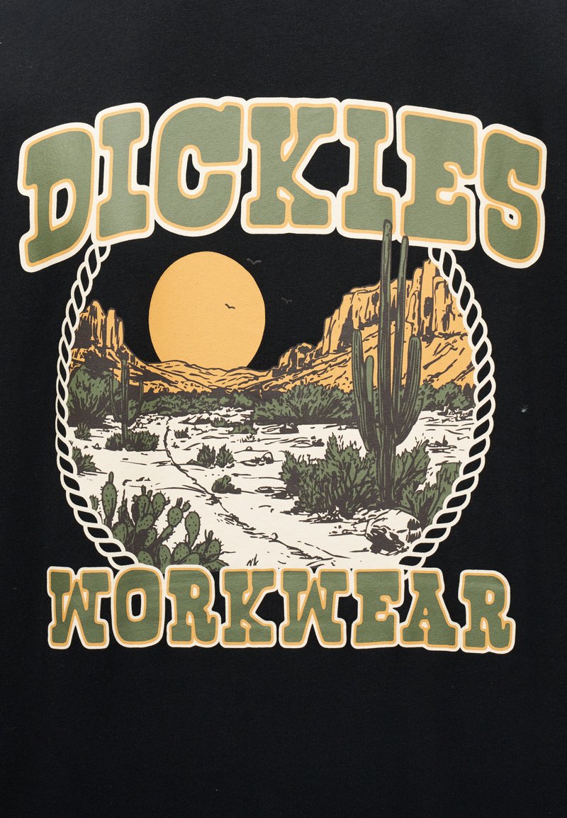 Paesaggio desertico con cactus, scogliere rocciose, un grande sole e uccelli, incorniciato da un cerchio di corda, con la scritta "Dickies Workwear" sopra e sotto.