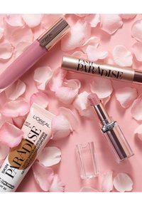 Trois produits L'Oréal : un gloss à lèvres rose mat, un tube de mascara or et noir, et une crème hydratante teintée, entourés de pétales de rose pink.