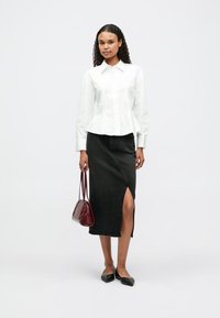 Chemise blanche à boutons avec une taille peplum, associée à une jupe en denim noire dotée d'une fente sur le côté. Accessoirisée avec un sac à main bordeaux.