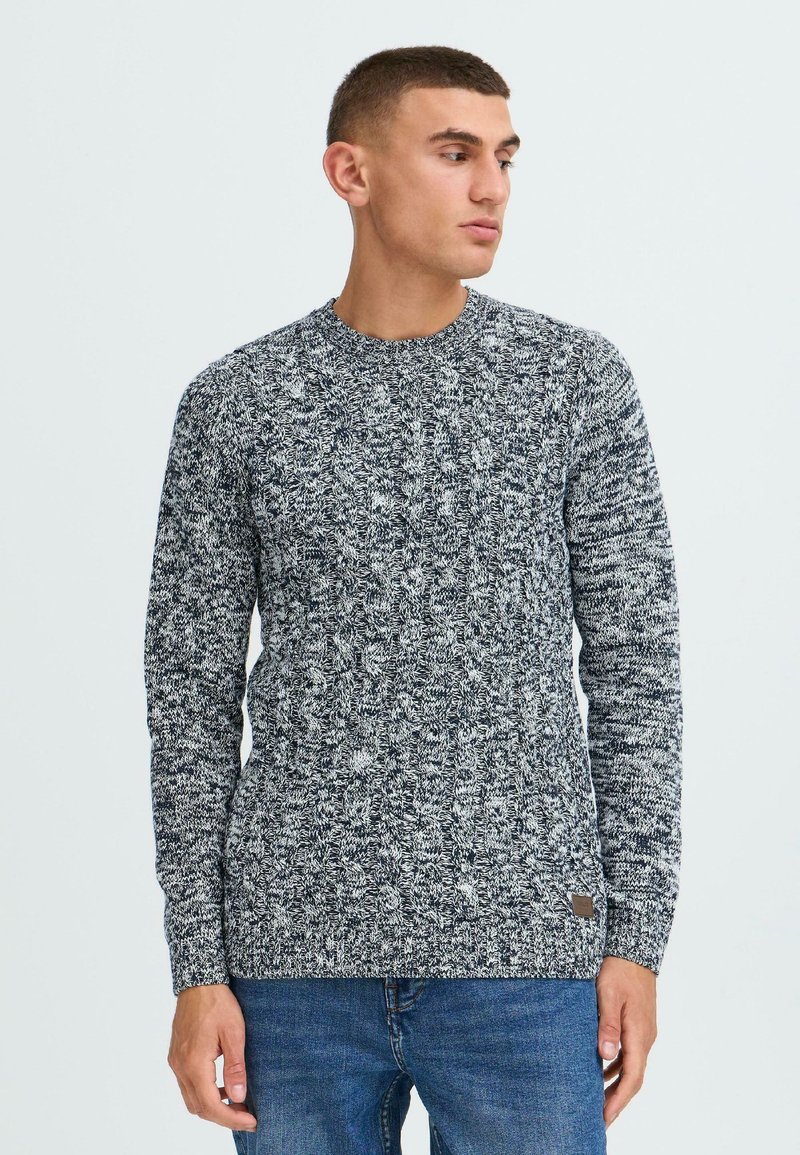Pulover tricotat cu un model texturat în navy și alb, cu guler rotund și mâneci lungi. Include o eticheta logo mică pe partea inferioară.