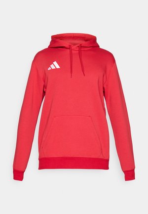 Crvena majica s kapuljačom s prednjim džepom, podesivim vezicama na kapuljači i bijelim Adidas logotipom na lijevoj strani prsnog koša. Izrađena od mekanog tkaninskog materijala s rebrastim manžetnama.