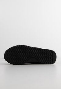 Podeszwa buta z czarną gumową bieżnią z falistymi wzorami, rozmiar 37, z małym strukturalnym logo blisko pięty.