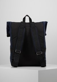 Černý a námořnicky modrý batoh s polstrovanými ramenními popruhy, designem s rolovacím uzávěrem a nastavitelným kováním. Vyroben z odolné, texturované látky.