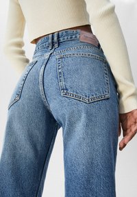 Jeans de mezclilla azul de cintura alta con un acabado desgastado, que cuentan con cuatro bolsillos y un parche de cuero en la parte posterior etiquetado "PULL&BEAR."