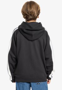 Sudadera con capucha negra que tiene rayas laterales en blanco y azul marino. Presenta un corte relajado, puños acanalados y una textura suave.