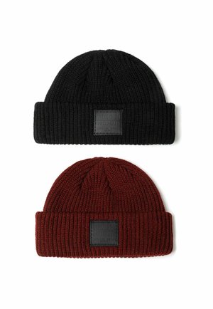 Zwei gestrickte Mützen: eine schwarze oben und eine dunkelrote darunter. Jede hat einen umklappbaren Bund und ein quadratisches Etikett auf der Vorderseite.