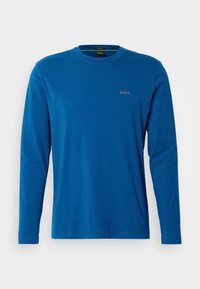 Långärmad blå skjorta i bomull. Har rund halsringning och en liten broderad logotyp på bröstet. Slät textur.