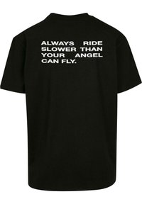 Sort bomulds T-shirt med en afslappet pasform, prydet med fed hvid tekst på ryggen, der står: "RIDE ALDRIG LANGSOMERE END DIN ENGEL KAN FLYVE."