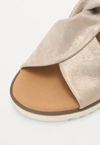 Sandale à enfiler beige métallique avec une tige texturée, de larges brides croisées et une semelle intérieure en tan rembourrée. Semelle en caoutchouc arrondie avec des détails sur les bords.