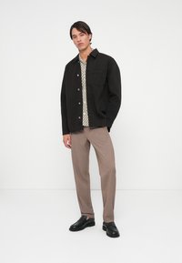 Crna jakna s dugim rukavima, košulja s uzorkom, bež hlače i crne cipele bez kopčanja. Jednostavan dizajn, glatka tekstura i kroj po mjeri.