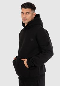 Zwarte hoodie gemaakt van zachte stof. Beschikt over een voorzak en ribgebreide manchetten. Subtiele branding gedrukt op de borst.
