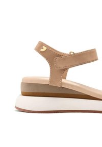 Sandalbeige con tomaia in pelle liscia, cinturino alla caviglia regolabile e suola a cuneo in schiuma stratificata con tonalità beige chiare e scure.
