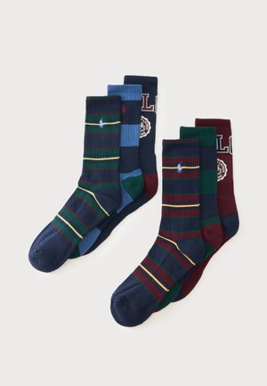 Deux paires de chaussettes montantes côtelées pliées avec des motifs rayés et petits logos en bleu marine, bleu, vert et bordeaux sur fond blanc.