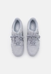 Grey athletic shoes with a perforated suede upper, smooth laces, and a cushioned insole, featuring the Asics logo on the tongue.