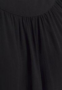 Tejido negro con detalles fruncidos, textura suave y un ligero brillo. El material parece ligero y flexible.