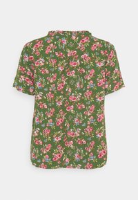 Blouse florale verte avec des manches courtes, un col à volants et un imprimé total de fleurs roses et bleues sur un tissu texturé.