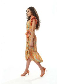 Orange and teal patterned midi dress with ruffled shoulders and a tie waist. Paired with orange high-heeled sandals.