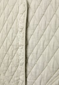 Gros plan sur un tissu matelassé beige avec un motif de couture en losange et une texture superposée.