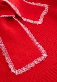 Punane kangas, millel on tekstureeritud pind, mille ümber on lai pitsist ääris kahe sümmeetrilise ala ümber, lisades dekoratiivset detaili.