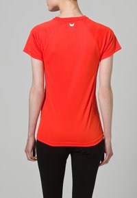 Camiseta deportiva roja de manga corta, con un cuello redondeado y un pequeño logo en la nuca. Fabricada con un tejido suave y elástico.