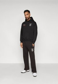 Zwarte hoodie met een voorzak en logo, gecombineerd met bijpassende zwarte joggingbroek. Inclusief witte sneakers met zwarte zolen.