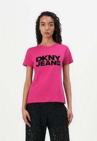 Lyhythihainen magentaväri t-paita, jossa on paksuilla mustilla kirjaimilla painettu "DKNY JEANS". Pehmeä kangas, pyöreä kaula-aukko ja rento istuvuus.