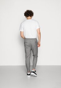 Calças cinzas às riscas com um corte ajustado, cintura elástica e sapatilhas pretas. T-shirt branca visível, cabelo encaracolado visto por trás.