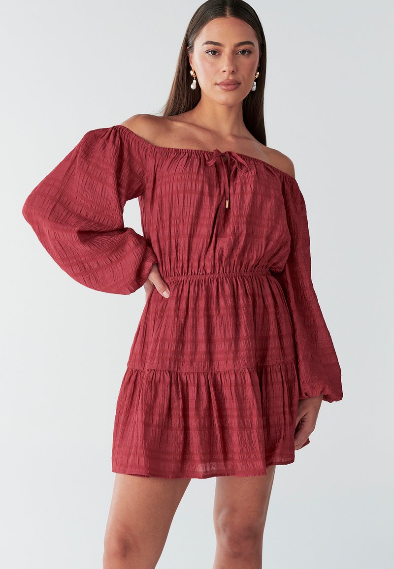 Rode off-shoulder jurk met lange mouwen, getailleerde taille, gelaagde rok en gestructureerde stof met subtiele verticale strepen.