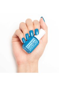 Vernis à ongles bleu dans un flacon en verre carré avec un capuchon blanc. Une main présente des ongles soigneusement manucurés dans une teinte bleue brillante assortie.