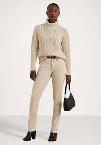Beige knitted turtleneck sweater with cable knit pattern, paired with beige fitted jeans. Black heeled ankle boots and a small black handbag.