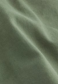 Gros plan sur un tissu vert pâle avec de fines côtes diagonales et de douces plis mettant en valeur la texture et le motif de tissage.