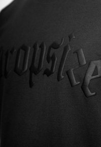 Camiseta de tela negra con letras en relieve y grabadas en un tono negro contrastante, que presenta una textura suave y un diseño moderno.