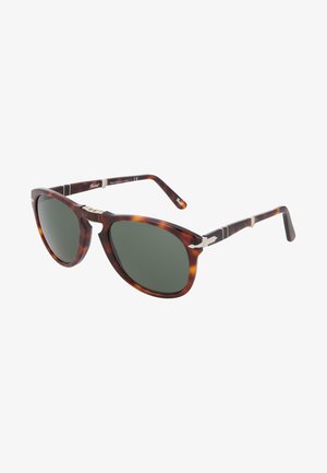 Óculos de sol em tartaruga com armações arredondadas, lentes verdes, detalhes metálicos nas hastes e um acabamento liso e brilhante. Feitos à mão na Itália.