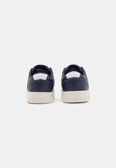 Zapatillas azul marino con acabado de cuero texturizado, acentos blancos en el talón y una suela de goma de color crema. Diseño minimalista, de corte bajo.