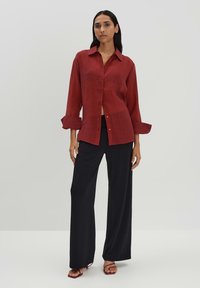 Camicia rossa in lino a maniche lunghe con bottoni e polsini arrotolati, abbinata a pantaloni morbidi neri a gamba larga. Tessuto morbido e vestibilità comoda.