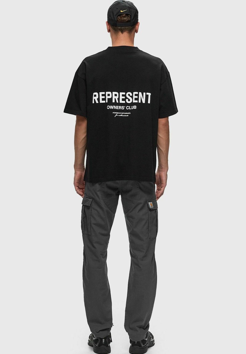 Camiseta negra con texto grande en blanco "REPRESENT" y "OWNERS' CLUB" en la parte de atrás, acompañada de pantalones cargo grises con bolsillos laterales.